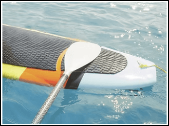 A paddle resting on the edge of a colorful stand-up paddleboard in clear blue water.