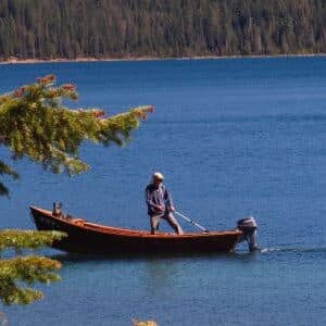 A person stands on a small wooden boat in a tranquil lake surrounded by trees.
