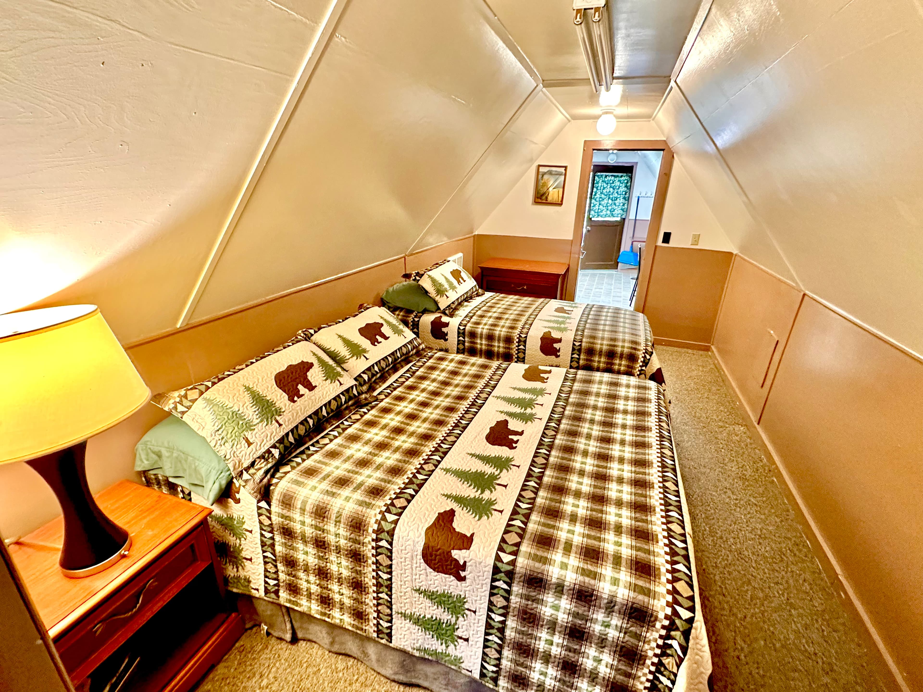 A cozy, A-frame bedroom with two beds adorned in bear-patterned blankets and a lamp beside them.