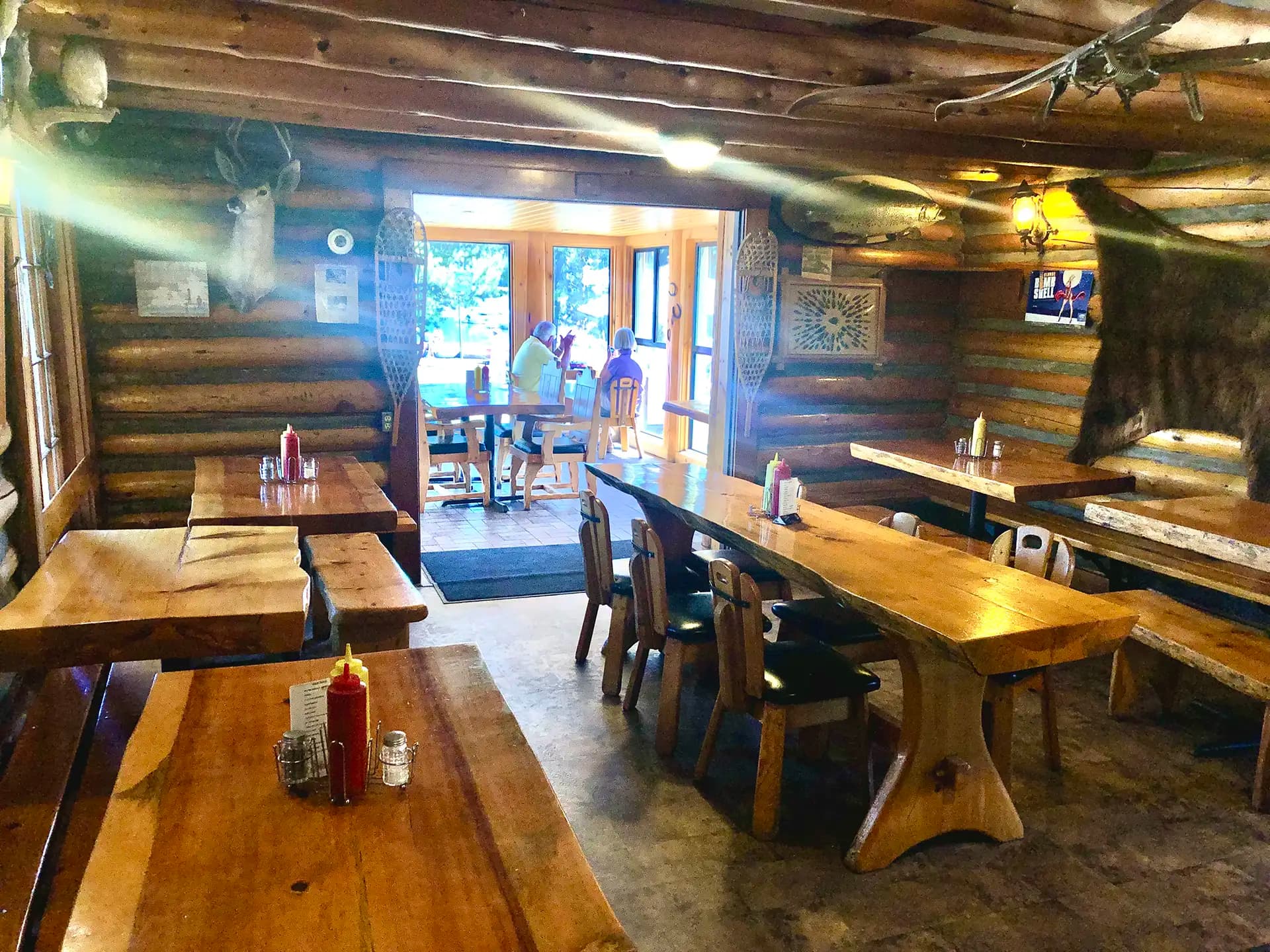 Interior of a rustic restaurant with wooden tables and a view of customers at the entrance.