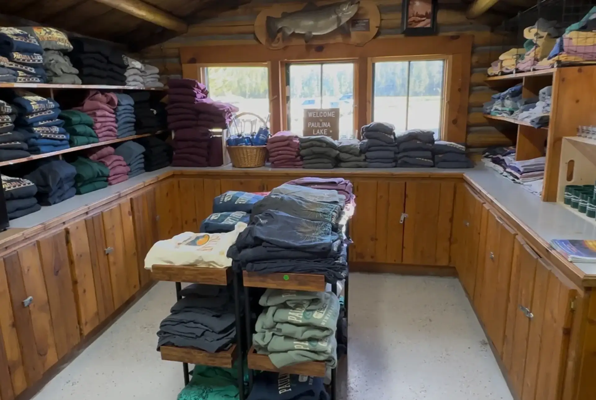 Interior of a cozy shop featuring neatly stacked clothing on wooden shelves and a display cart.