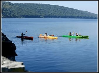 Four people kayaking on a calm lake with green hills in the background.