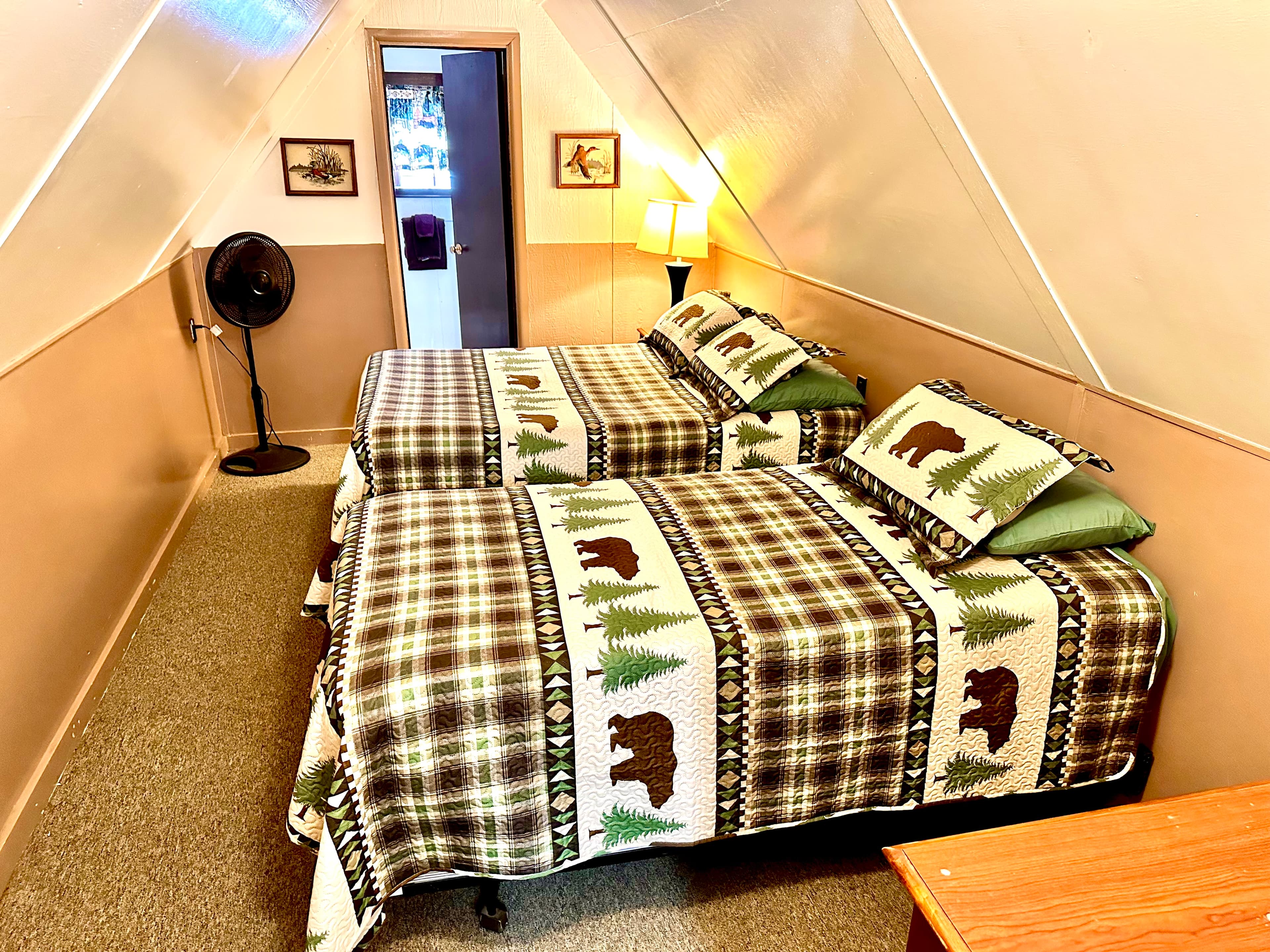 A cozy attic bedroom featuring two beds with bear-patterned blankets and a wooden dresser.