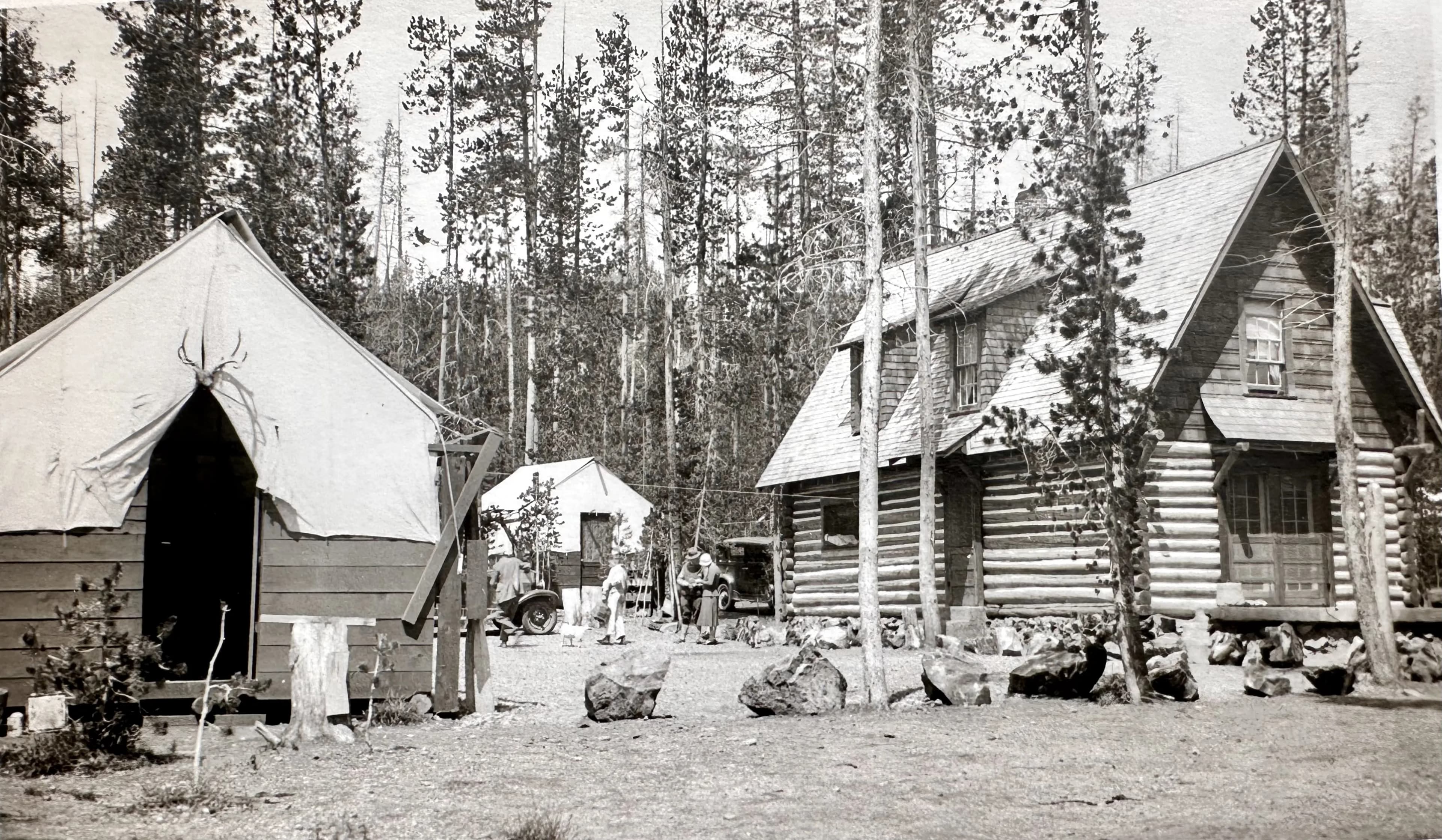 Historic campsite featuring tents and log cabins surrounded by trees.
