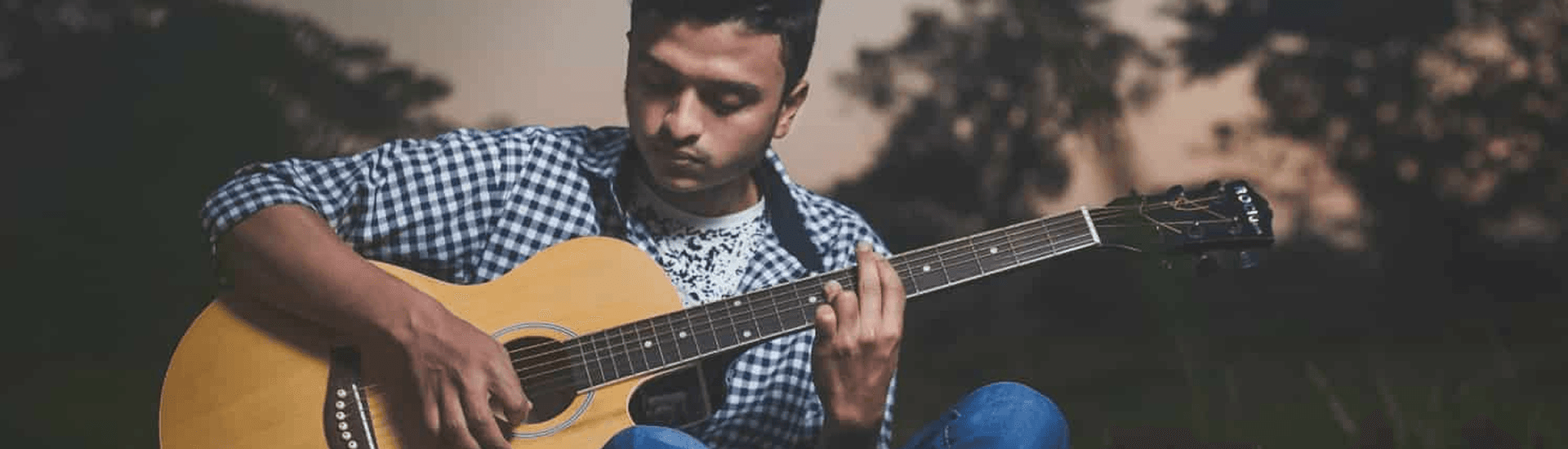 A man sits outdoors playing an acoustic guitar.