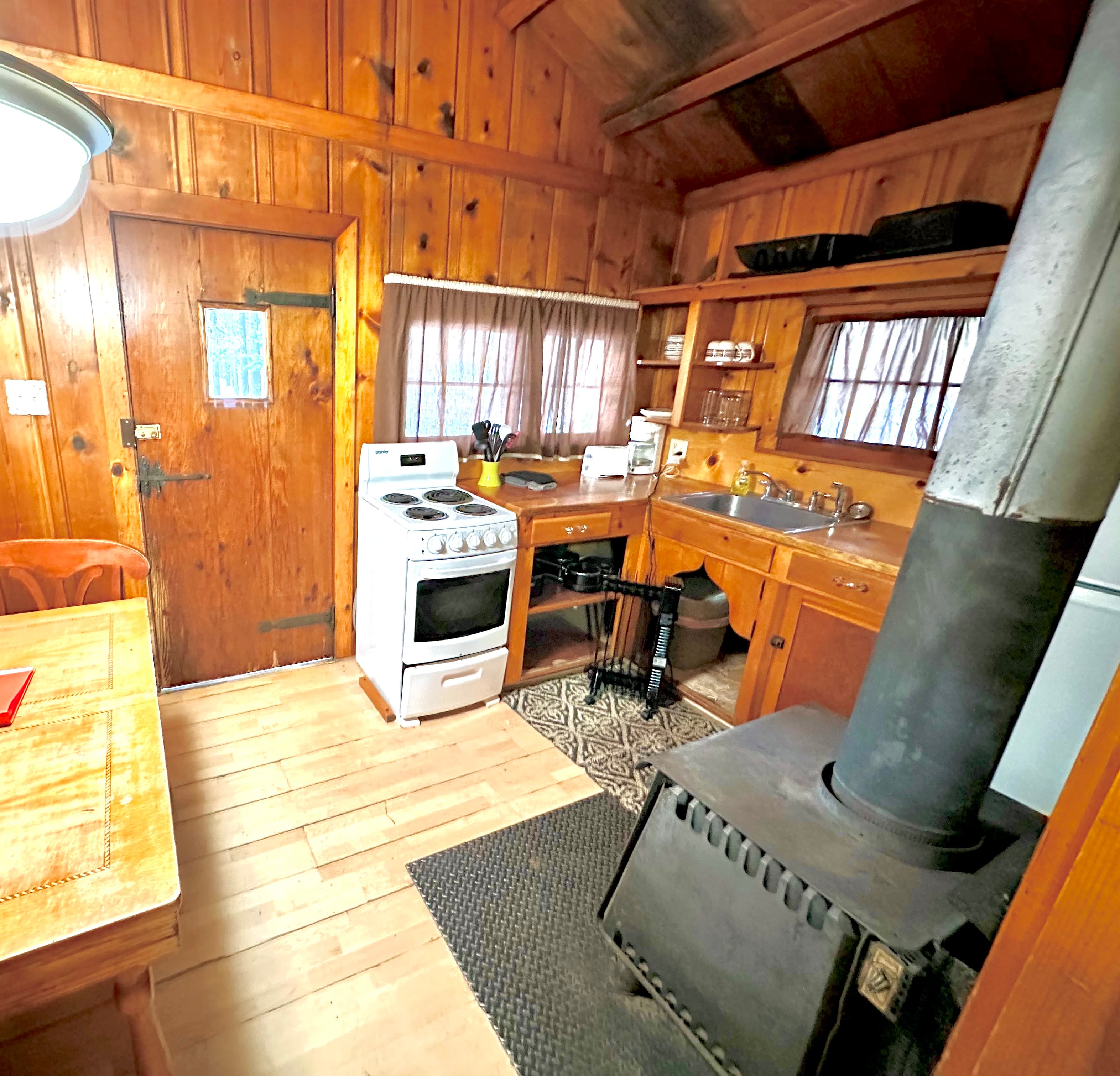 Cozy wooden kitchen with a stove, sink, and a table in a rustic cabin setting.
