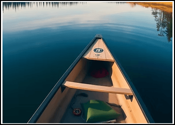A canoe glides across a calm lake surrounded by trees and reflections.