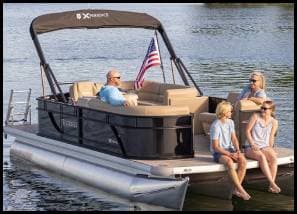A family enjoys a relaxing day on a pontoon boat with seating and an American flag.