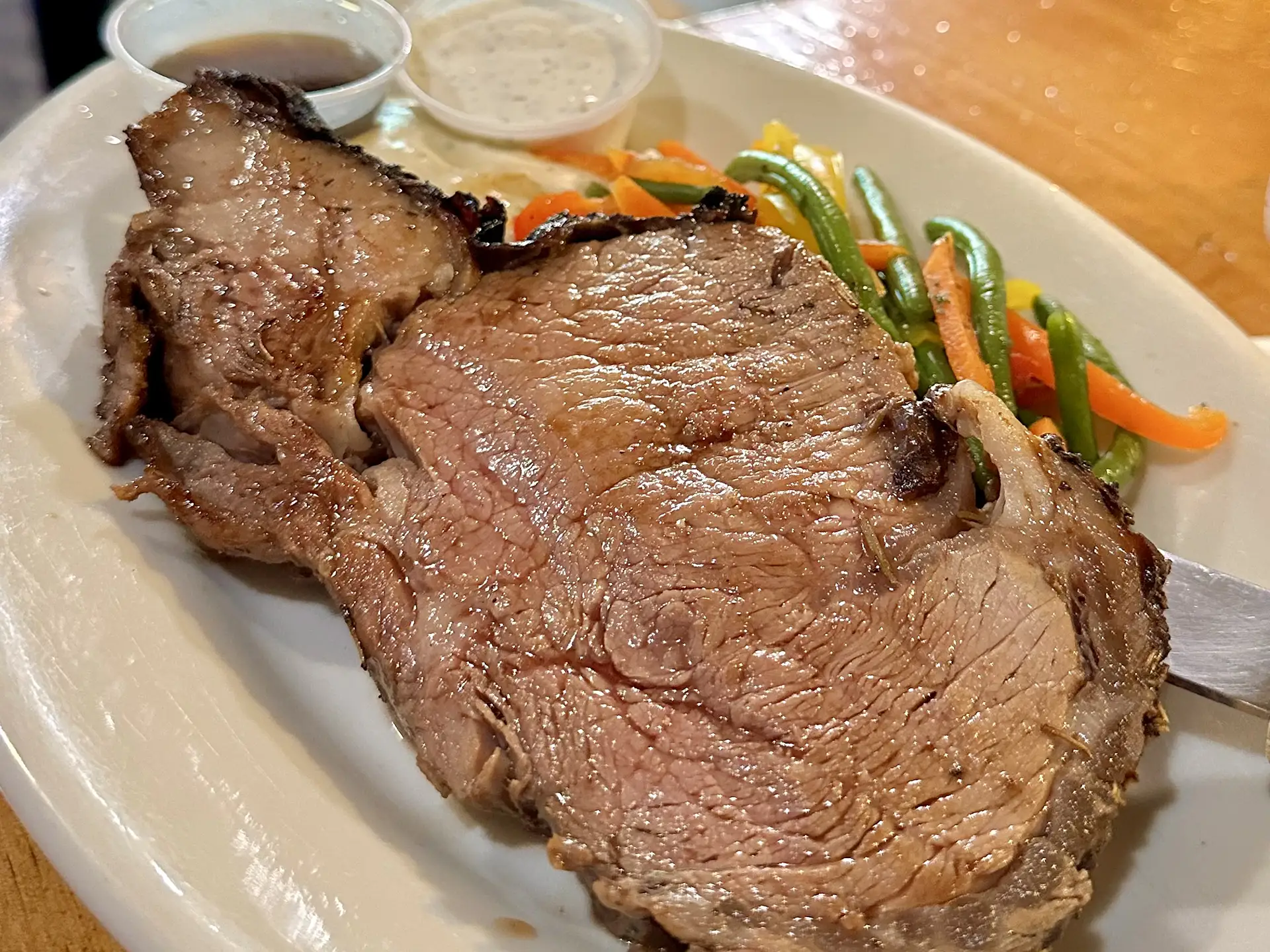 A large slice of prime rib served with vegetables and dipping sauces.