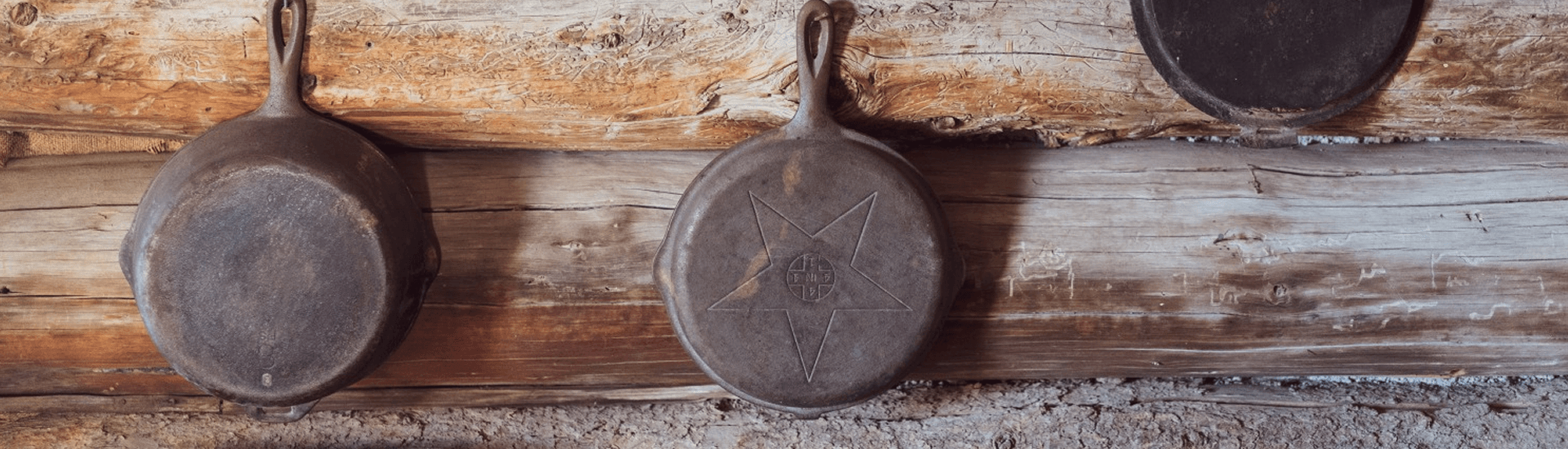 Two vintage cast iron skillets hanging on a rustic wooden wall.